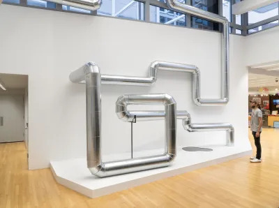 A man staring at a bending and looping metal pipe in a gallery.