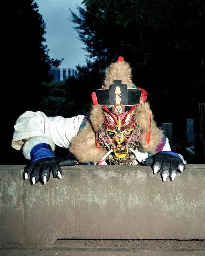 A person wearing a dragon-like mask pretending to crawl over a wall.