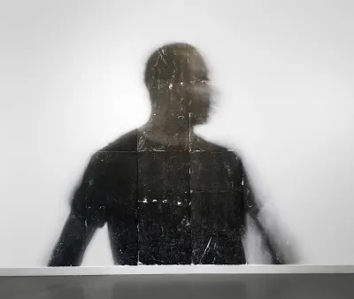 A photograph showing a Black person whose head is blurred as they turn their head and arm.