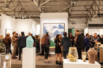 A group of people moving through the aisle of an art fair.