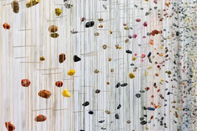 View of several pebbles hang from strings near a wall. 