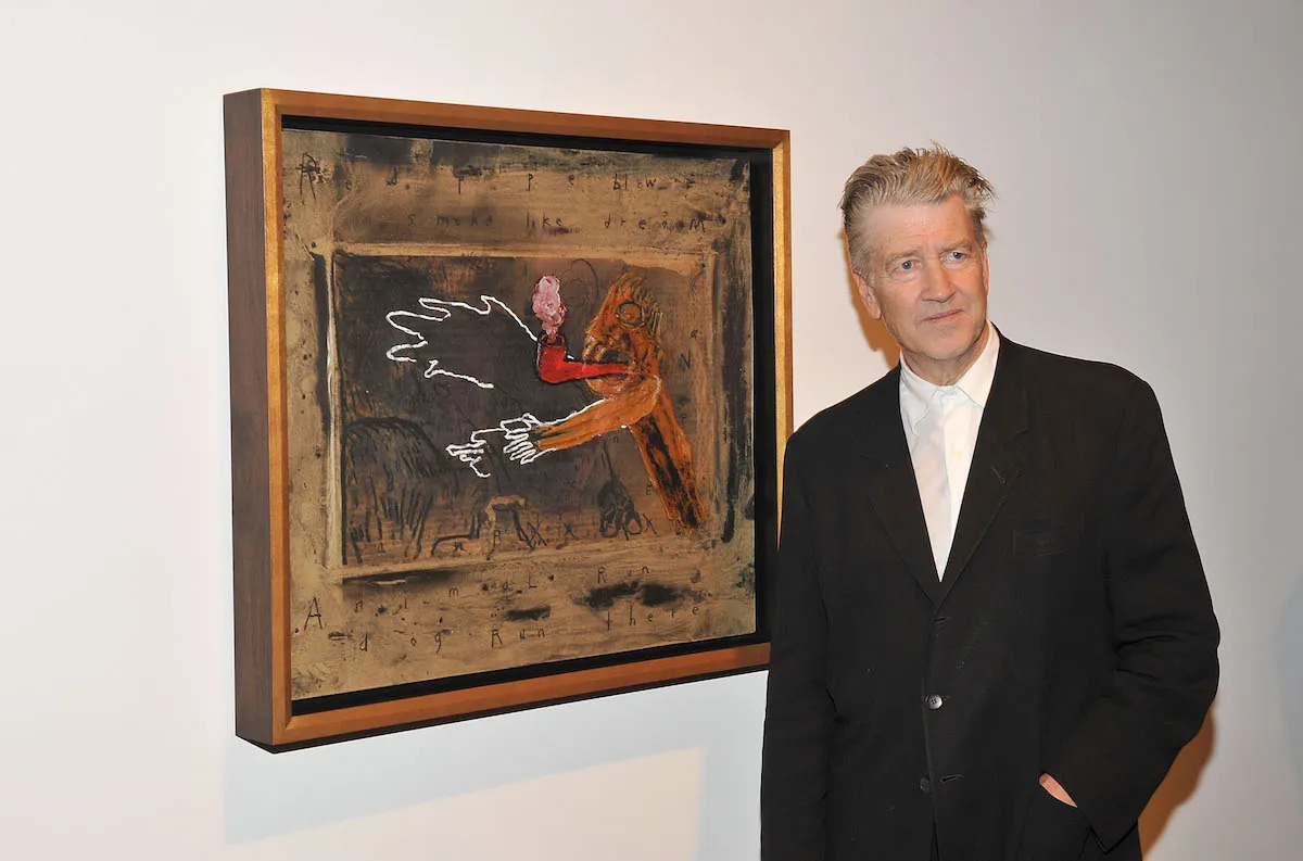 A man in a suit beside a painting of a smoking pipe and hands.