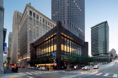 A boxy building set amid skyscrapers on a city street.