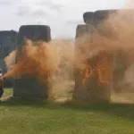 Two protestors spray orange powder paint on the Stonehenge monument.