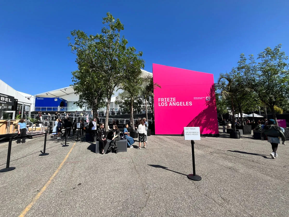 A pink sign that reads Frieze Los Angeles in a parking lot with a tent behind it.