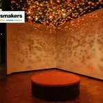 An installation of orange petals hangs from the ceiling and is dramatically lit.