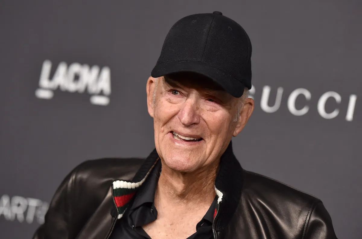 A smiling man wearing a black baseball cap and a leather jacket.