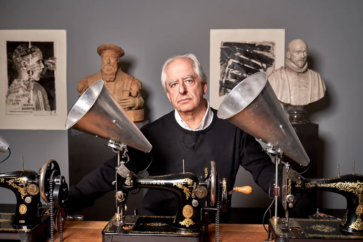 Portrait of William Kentridge, with two theater lights, three old-school Singer sewing machines, and two busts behind him.
