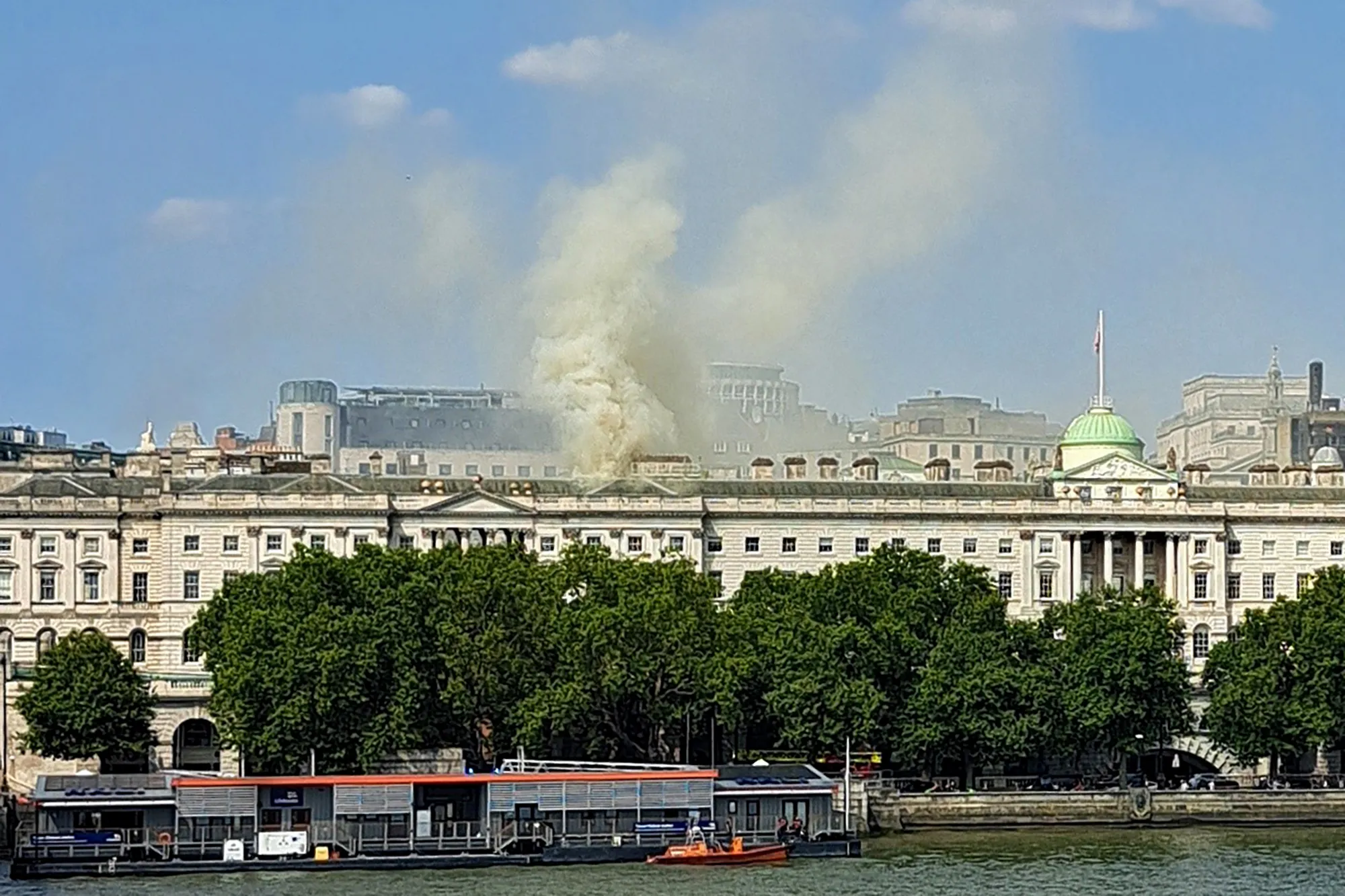 Smoke rising from the roof of a building near a river.