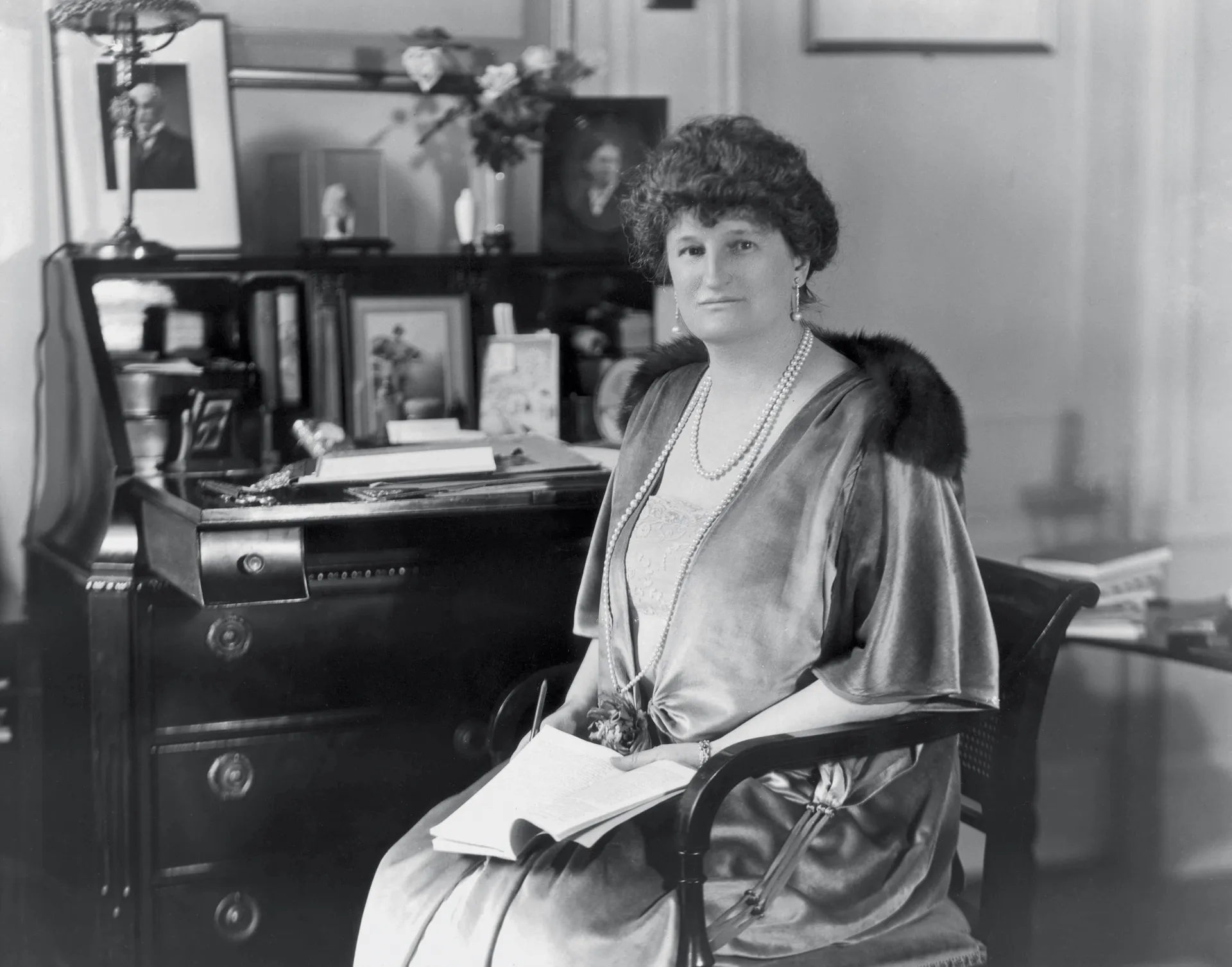 An archival black-and-white photograph of a rich white woman seated in front of a writing desk.