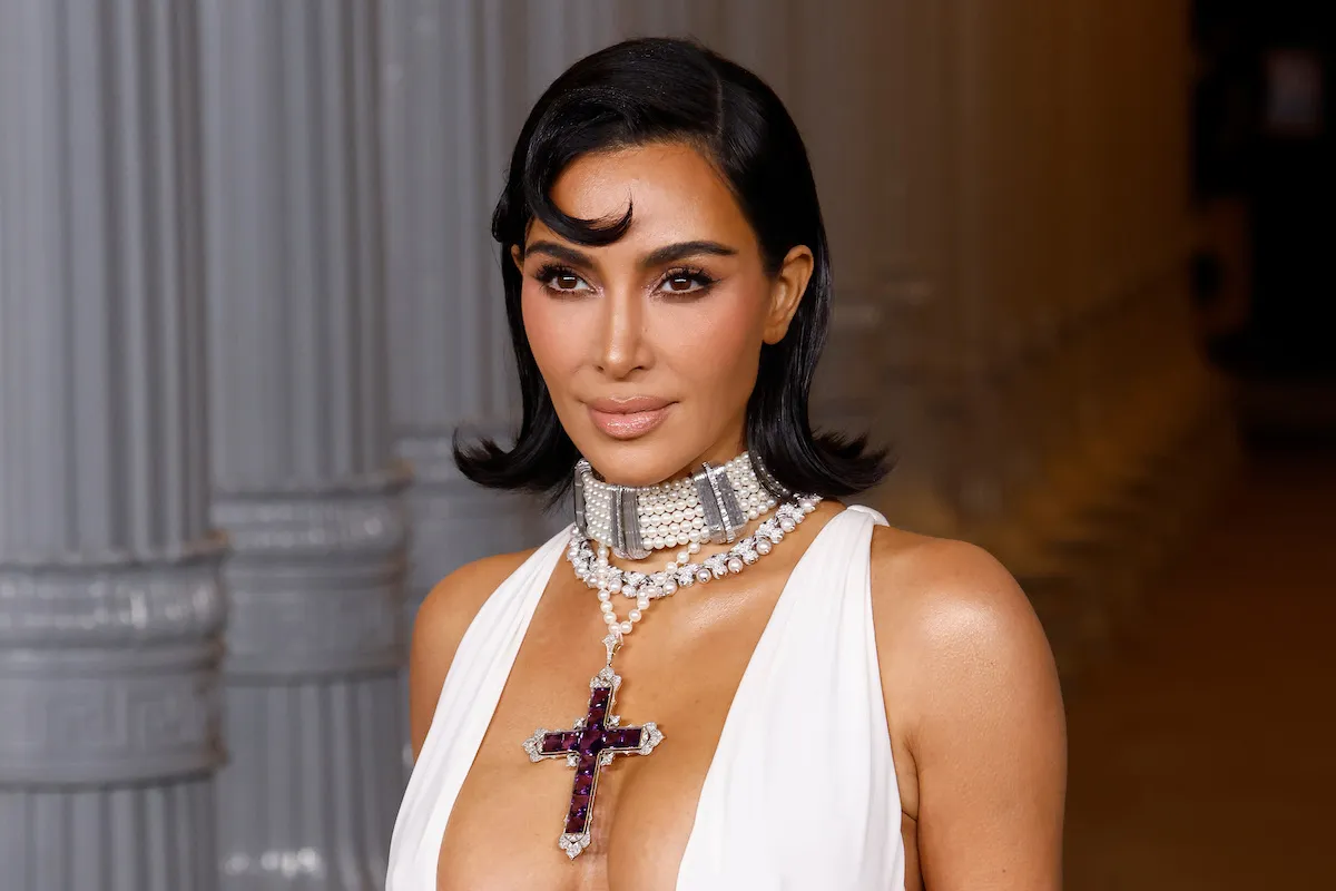 A smiling woman in a white dress wearing a cross-shaped necklace.