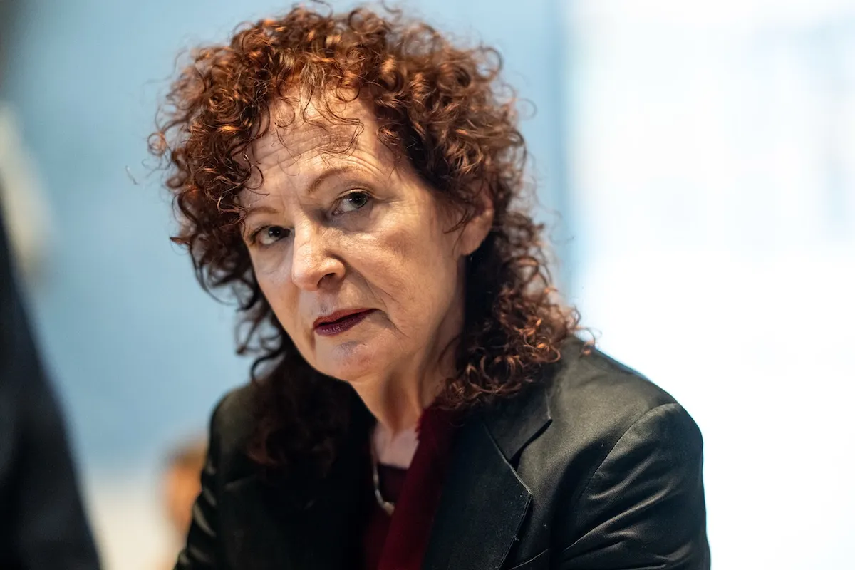 A white woman with curly red hair wearing a suit jacket.